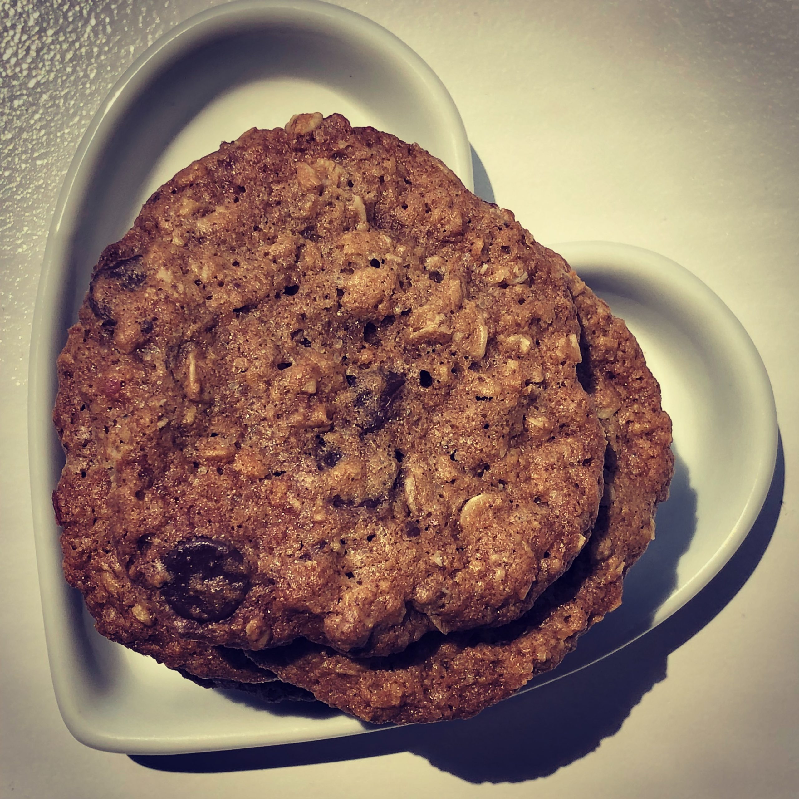 Chewy oatmeal chocolate chip and cranberry cookies on a white heart shaped container.